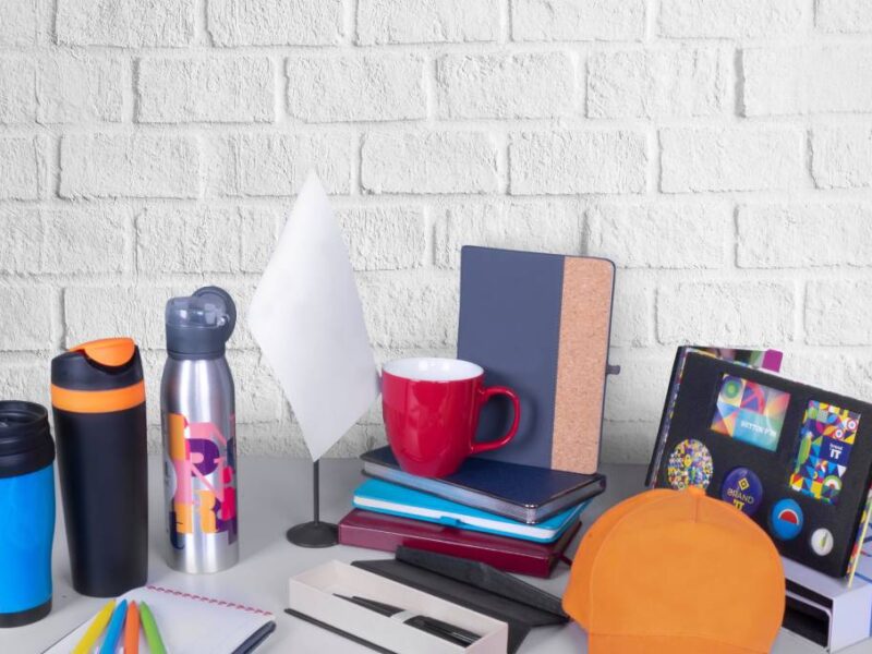 A variety of promotional products, like journals and cups, arranged with ample copy space against a grey wall background