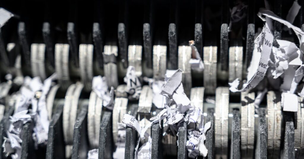 An extreme close-up view shows the metal teeth of a shredder. The teeth are shredding white paper.