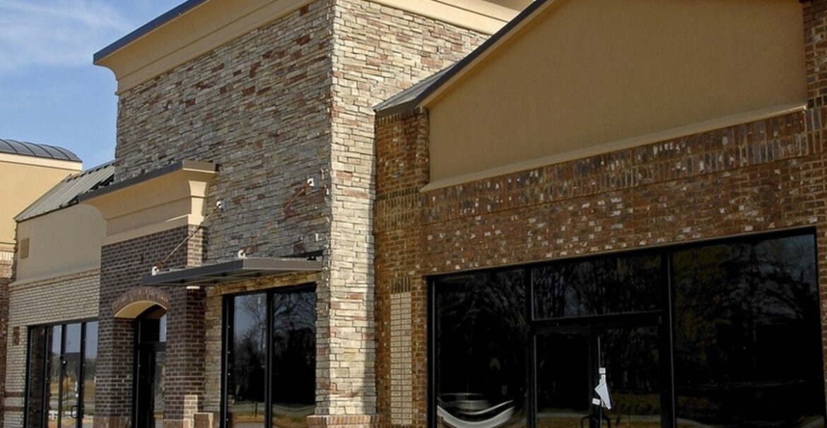 An empty commercial property with multiple connected storefronts. The windows and doors of the shops are tinted.
